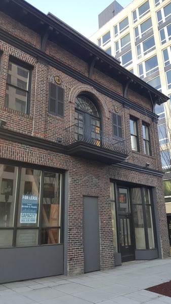 Historic brick building with arched windows and wrought-iron balcony, currently available for lease, contrasting with… — Northwest District, Portland
