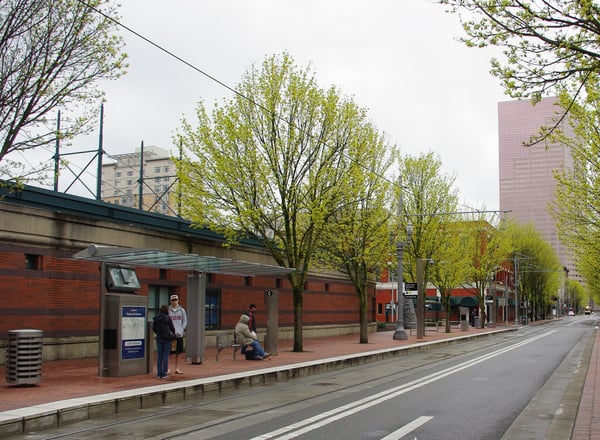 Transit station platform with red brick architecture, spring trees, and downtown Portland skyline in background. — Pearl District, Portland