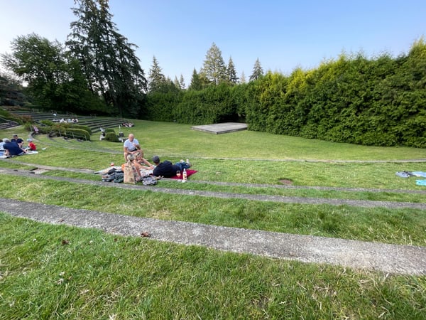 Visitors enjoying a sunny day in a manicured park with expansive lawns, coniferous trees, and amphitheater seating in… — International Rose Test Garden, Portland