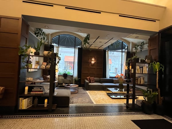 Modern hotel lobby with contemporary furnishings, potted plants, and large arched windows overlooking a street. — Downtown, Portland