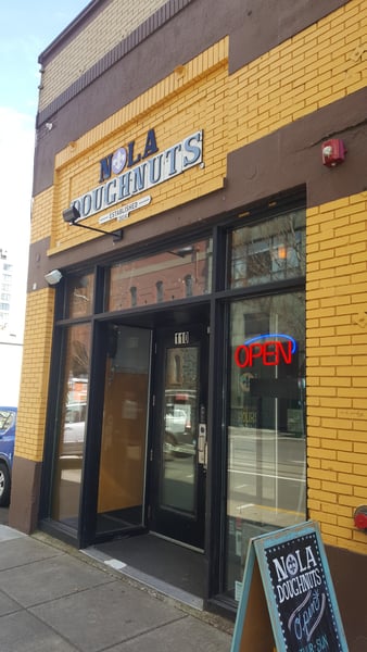 NOLA Doughnuts storefront with yellow brick facade and open sign on a city street in Portland, Oregon. — Old Town, Portland