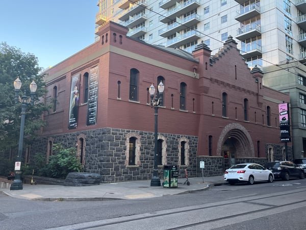 Historic red brick building with stone foundation and arched entrance, surrounded by modern high-rise apartments in an… — Downtown, Portland