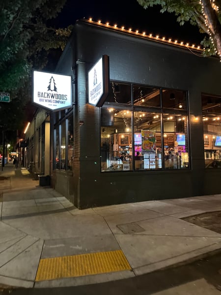 Backwoods Brewing Company storefront illuminated at night on a downtown street corner. — Pearl District, Portland