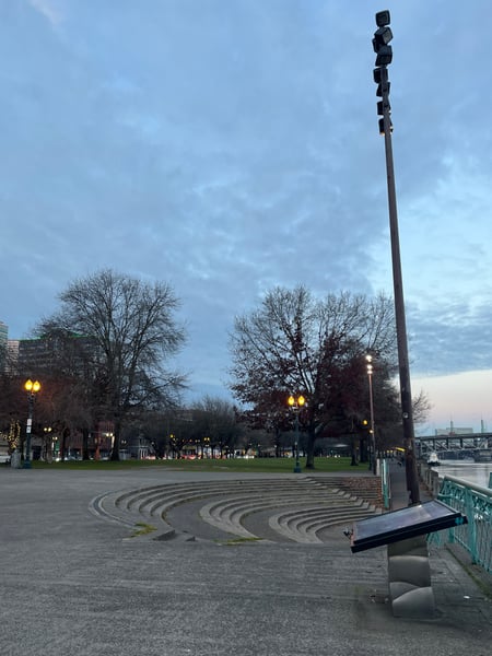 Tom McCall Waterfront Park at dusk with spiral plaza, tall light pole, and bridge visible across the river. — Old Town, Portland