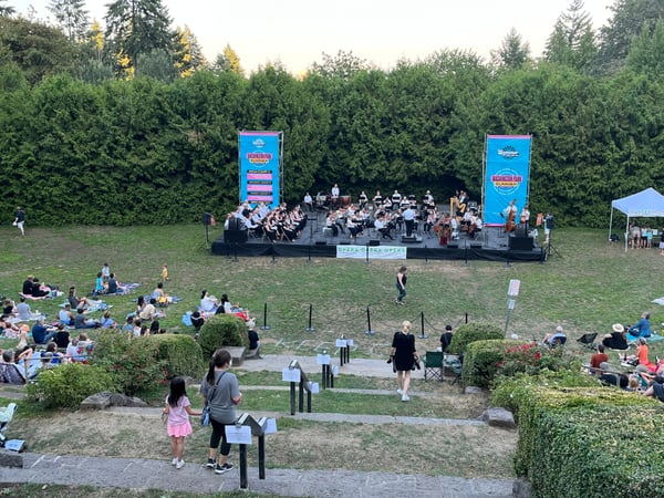 Outdoor opera performance at Washington Park with audience seated on lawn surrounded by evergreen trees and hedges. — International Rose Test Garden, Portland