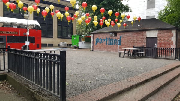 Urban plaza decorated with red and yellow lanterns, featuring a brick building with 'portland' signage and outdoor… — Downtown, Portland