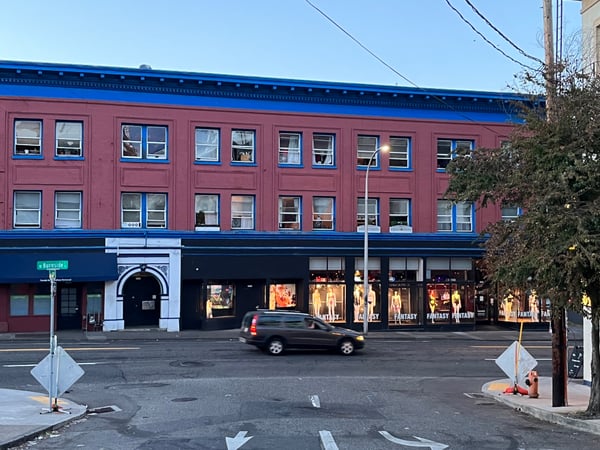 Red brick building with blue trim and ground-floor retail on Burnside Street, Portland, featuring a clothing store with… — Goose Hollow, Portland