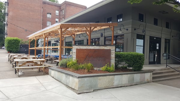 Outdoor dining patio with wooden pergola and picnic tables at a restaurant in an urban courtyard setting. — Downtown, Portland