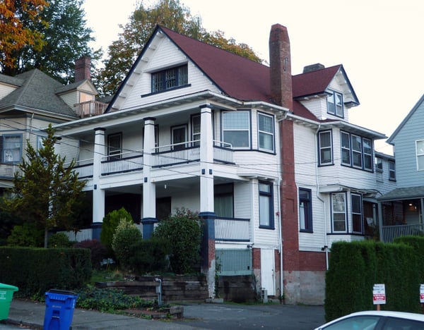 Early 20th-century residential house with white clapboard siding, red brick chimney, and wraparound porch in a historic… — Northwest District, Portland