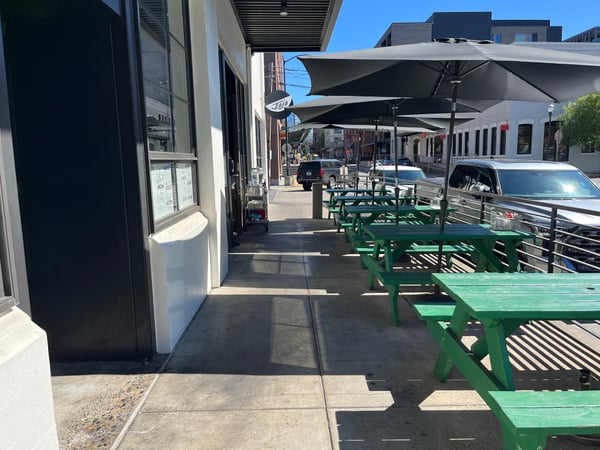 Outdoor patio seating with green benches and black umbrellas on a downtown street lined with brick buildings and parked… — Pearl District, Portland