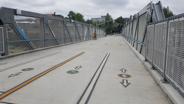 Modern pedestrian bridge with directional markings and metal mesh railings crossing over an urban area. — Northwest District, Portland