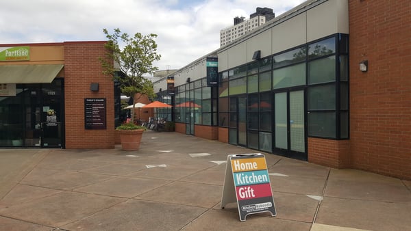 Thiele's Square shopping courtyard in Portland with retail storefronts, orange umbrellas, and a Home Kitchen Gift sign. — Goose Hollow, Portland