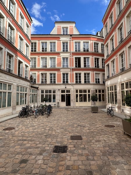 Haussmann-style courtyard in Paris with red and cream facades, bicycles parked on cobblestone ground, viewed from… — 11th Arrondissement, Paris