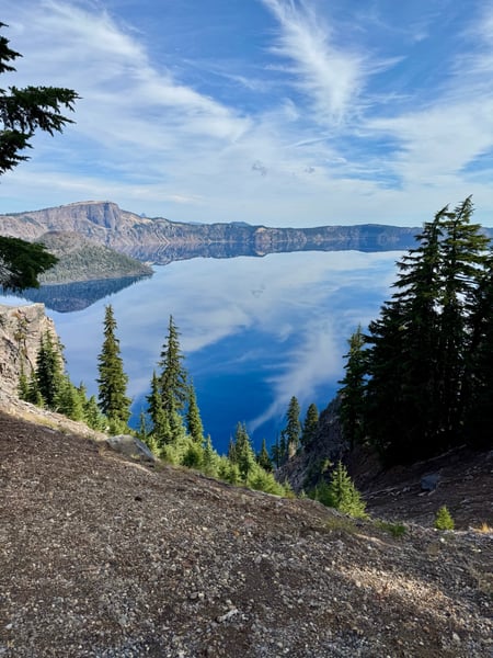 Crater Lake viewed from a volcanic rim with coniferous forest in the foreground and snow-capped caldera walls reflected… — Crater Lake National Park